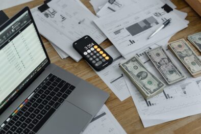 raamatupidamisteenuse hind kajastub arvutiekraanil, kõrvuti kalkulaatori, finantsdokumentide ja Ameerika dollari rahapakkidega laual